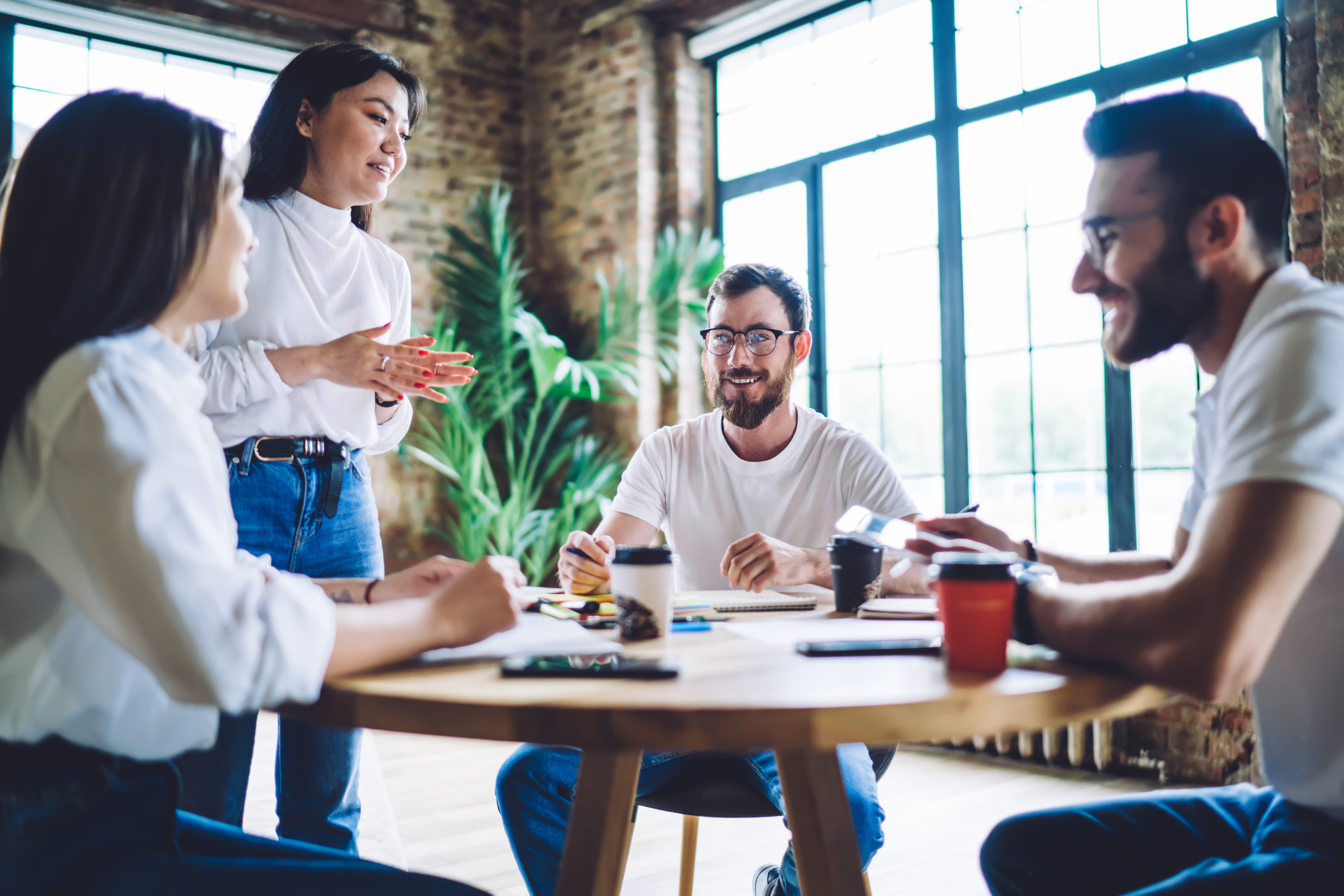 Positive young diverse managers sitting at table with takeaway coffees during meeting in workspace Positive young diverse managers sitting at table with takeaway coffees during meeting in workspace